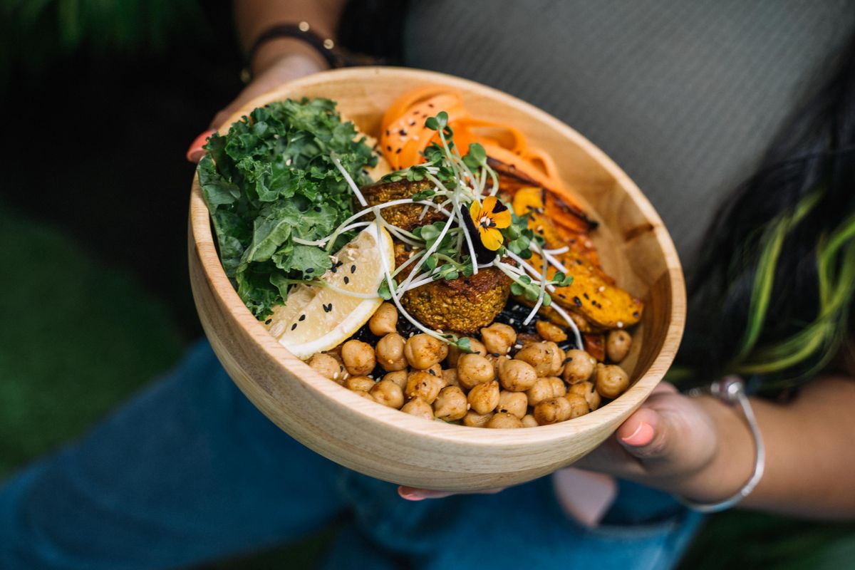 A bowl of chickpeas, leafy greens, carrot and lemon held in two hands.
